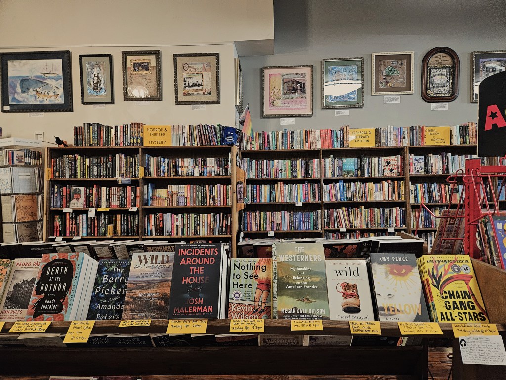 Interior of a bookstore with shelves in the background and a row of books in the foreground. 